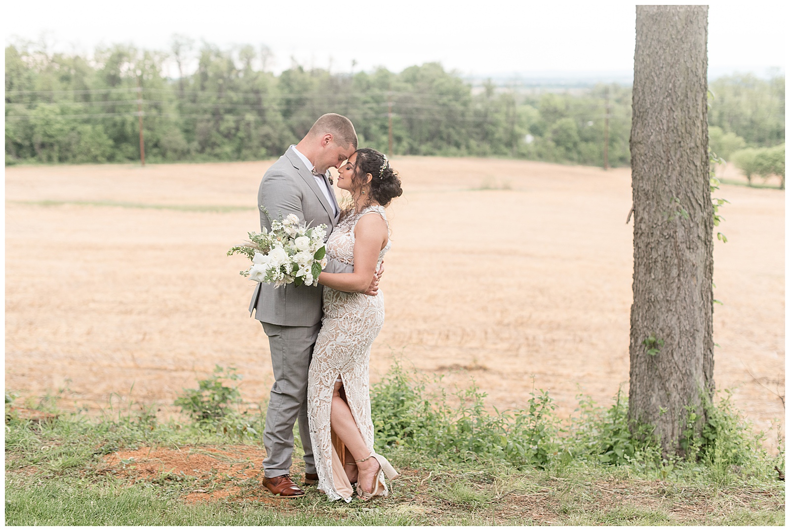 groom and bride hugging tightly and resting foreheads together beside tree near farm field in columbia pennsylvania