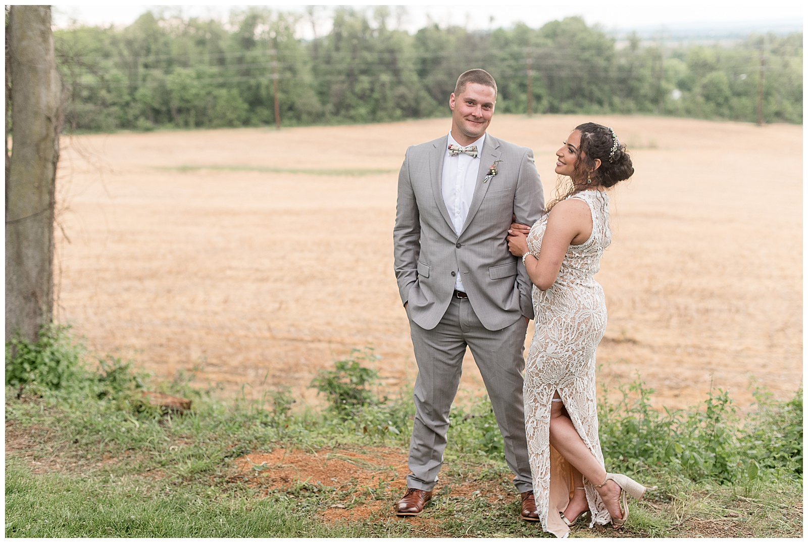 groom smiling at camera as bride wraps arms around his left arm while smiling at him near field in columbia pennsylvania