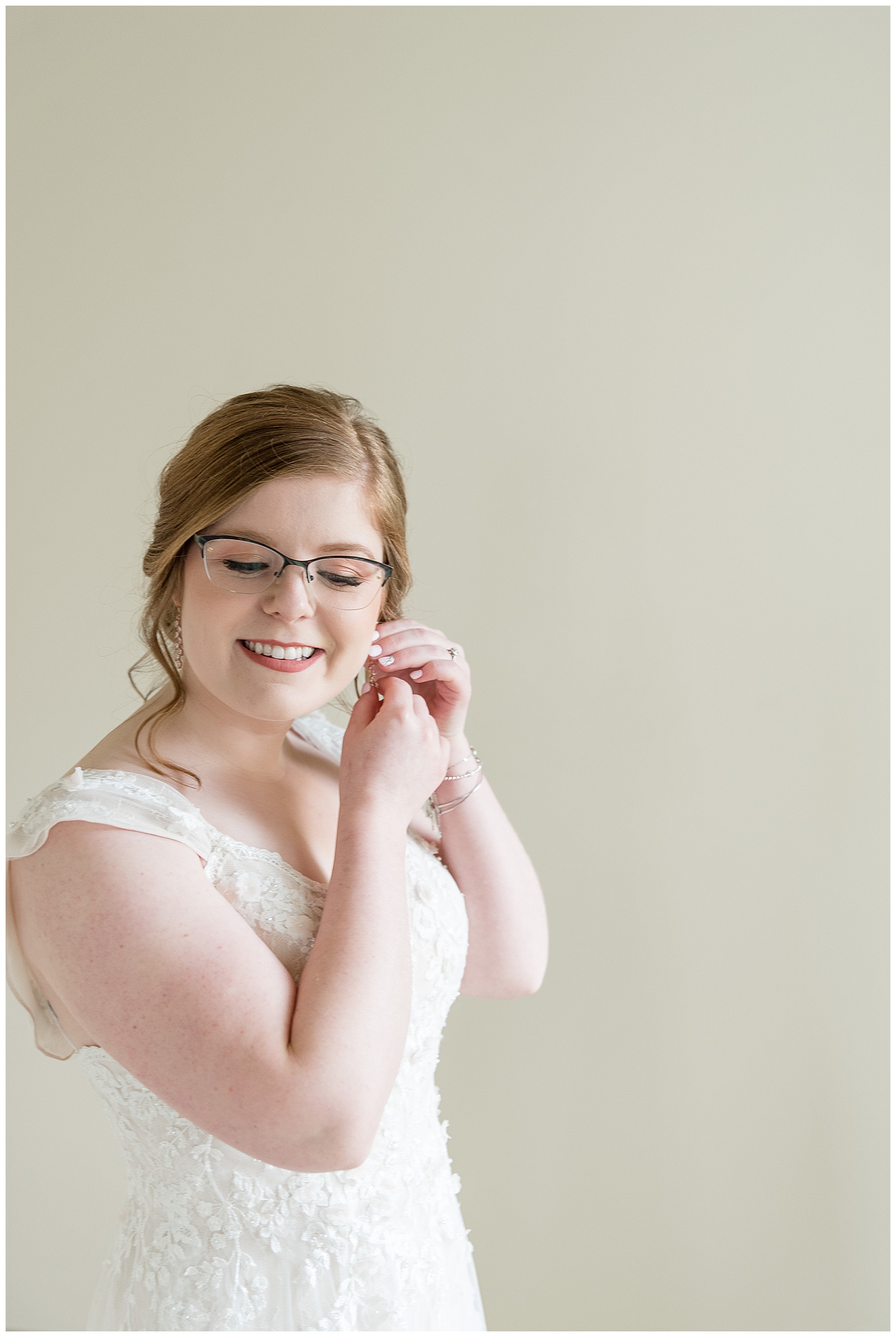bride making final touches with earring and looking down smiling in bridal suite in lancaster pennsylvania