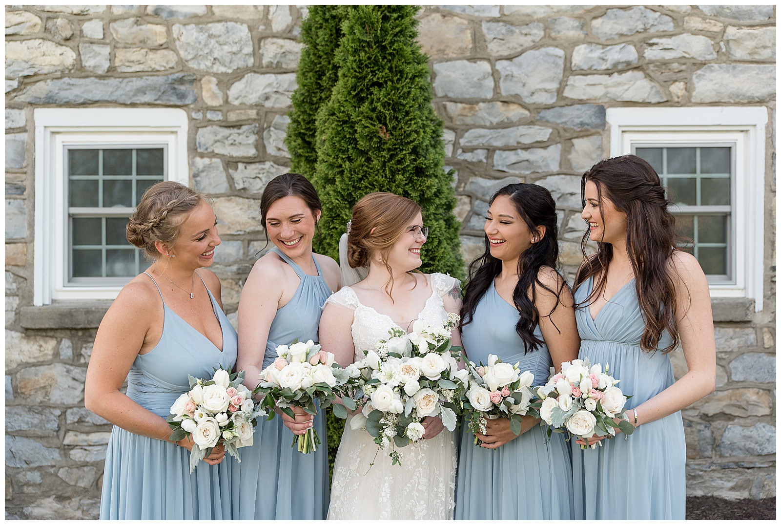 close up of bride and bridesmaids look at each other and smile while holding bouquets outside farmhouse at the barn at silverstone