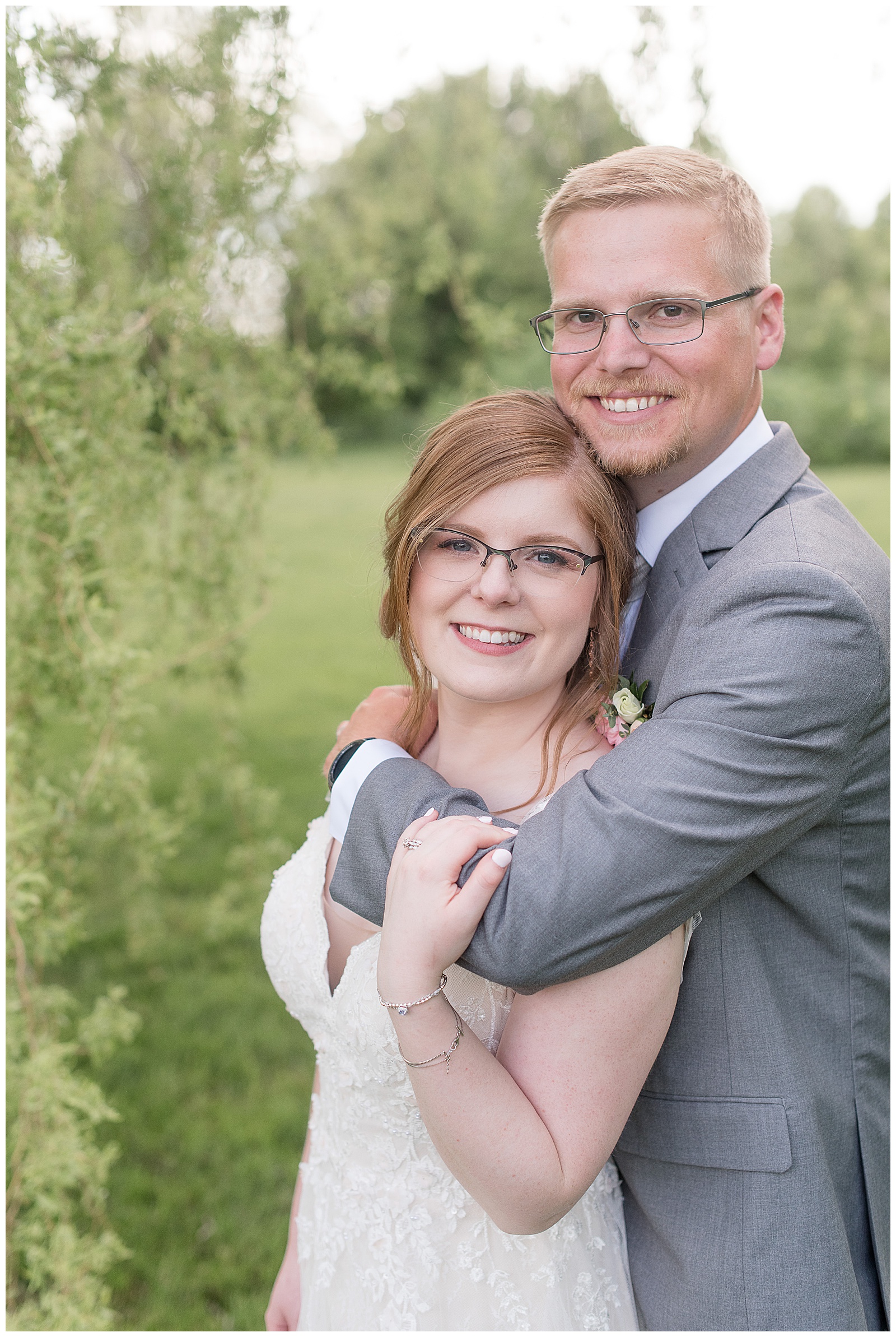 groom hugs bride tightly from behind and couple smiles while standing in meadow at the barn at silverstone