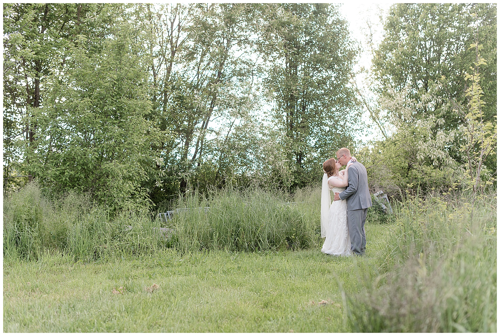 bride and groom kiss will standing in meadow of tall grasses on spring evening at the barn at silverstone