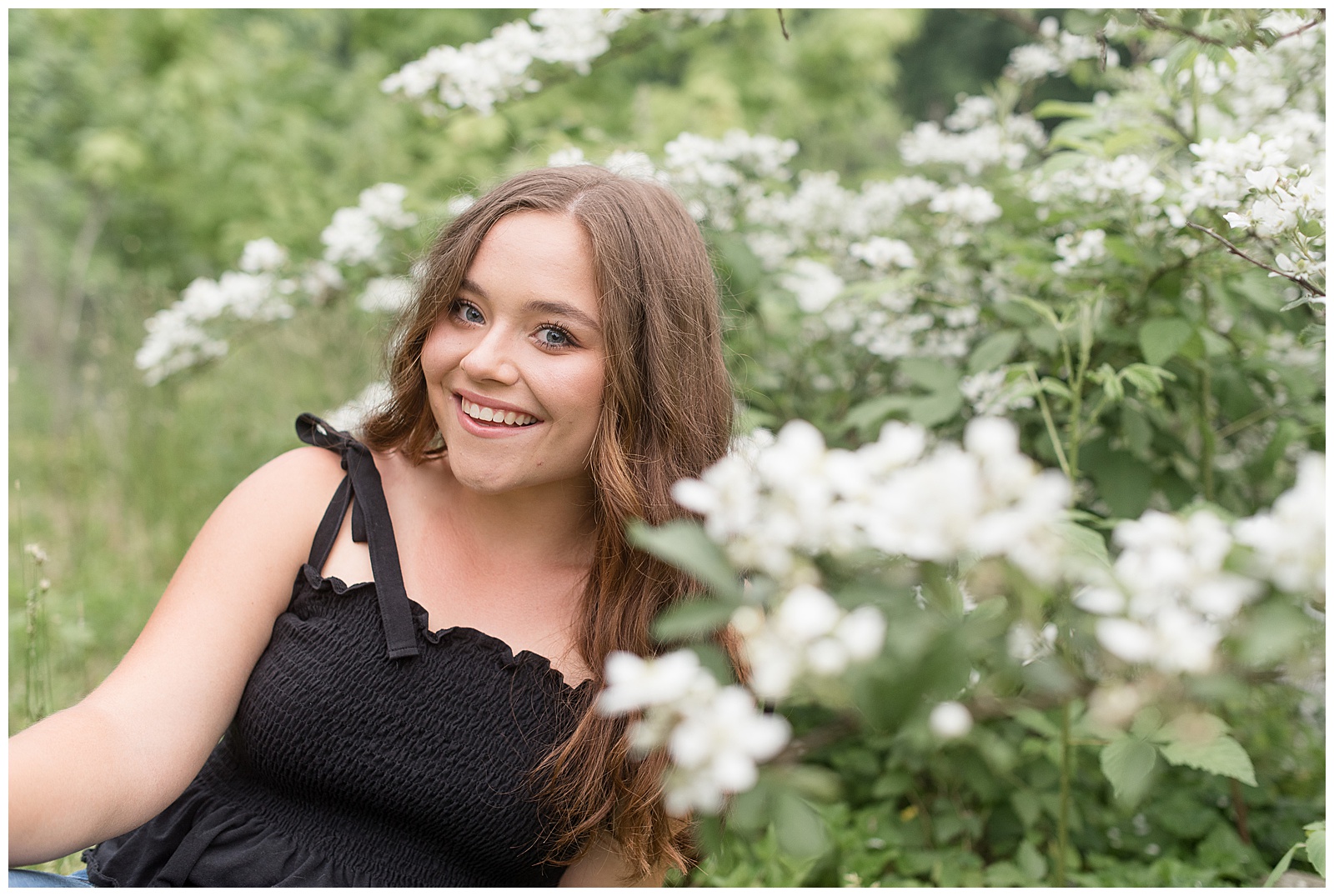 senior girl leaning in to white blooming bush and smiling at speedwell forge lake in pennsylvania