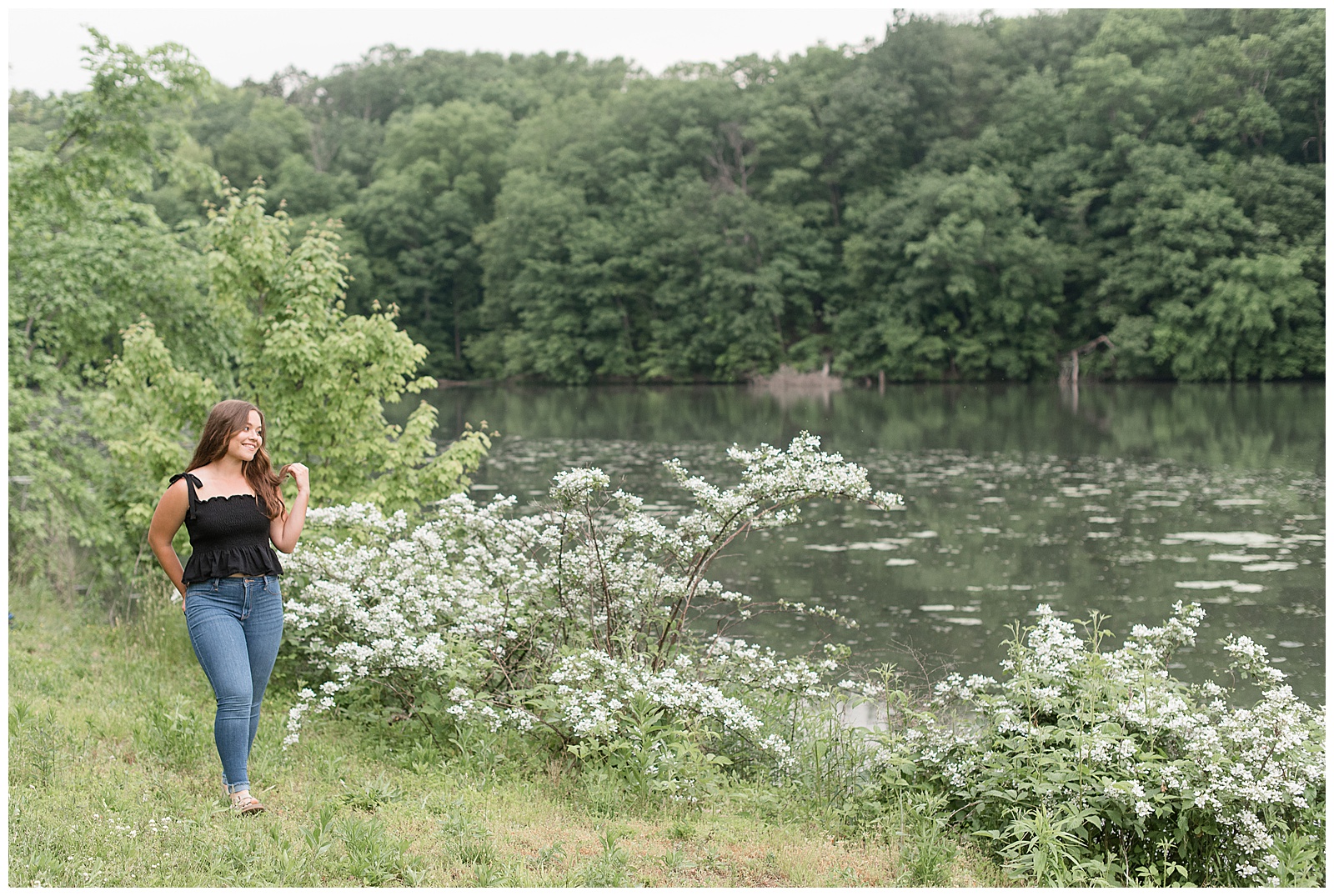 senior girl walking along lake and looking out at it with left hand going through her hair in lititz pennsylvania