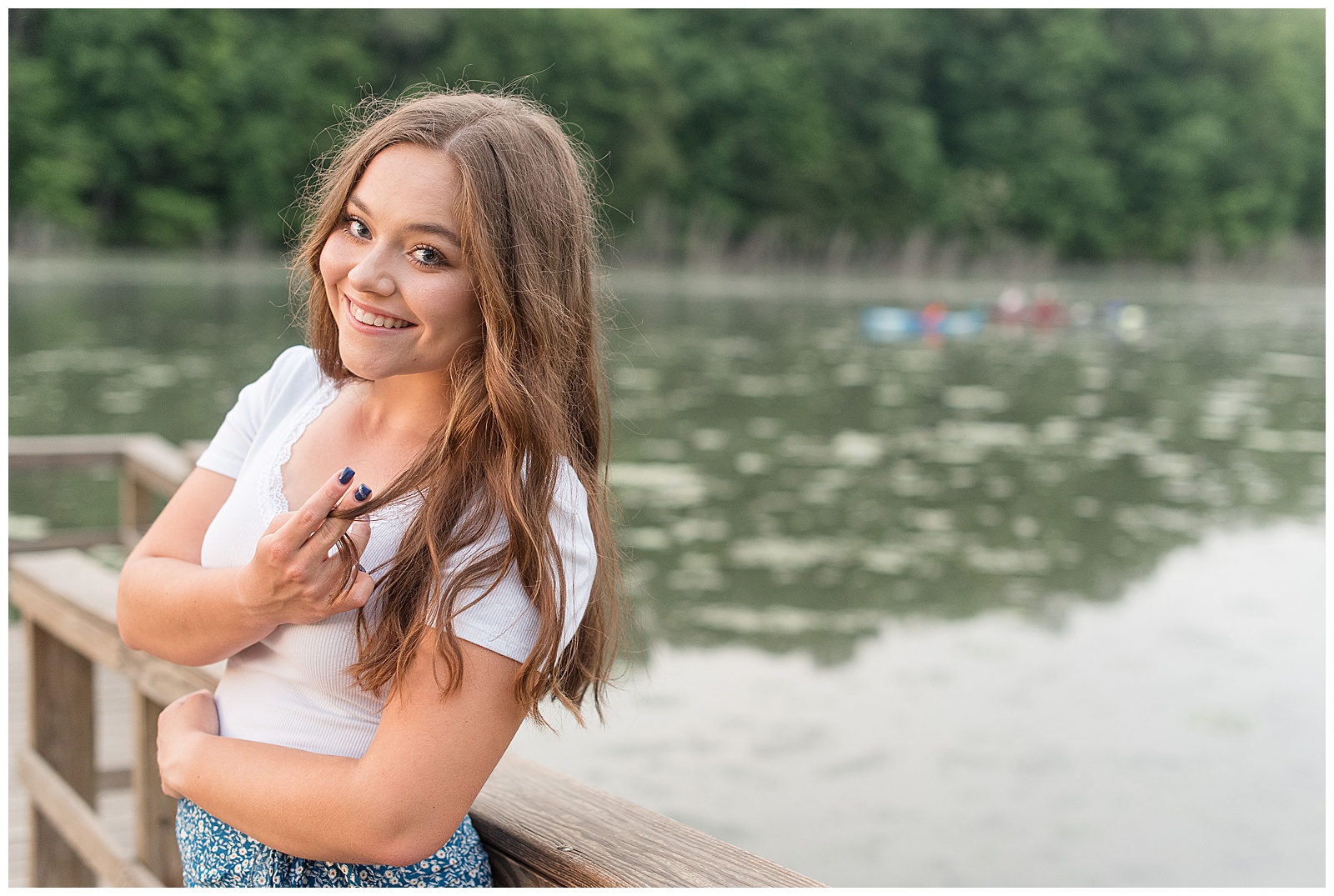 senior girl wearing white t-shirt and jeans leaning back against wooden rail at speedwell forge lake