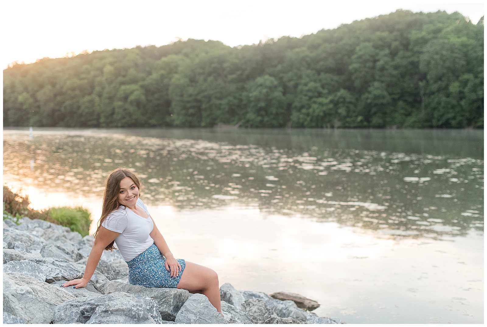 senior girl sitting on large rocks leaning back on right hand with sun setting on speedwell forge lake in pennsylvania