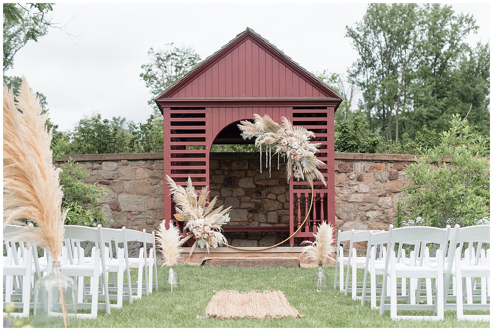 small maroon barn structure with floral archway at outdoor wedding ceremony area with rows of white chairs in lititz pennsylvania