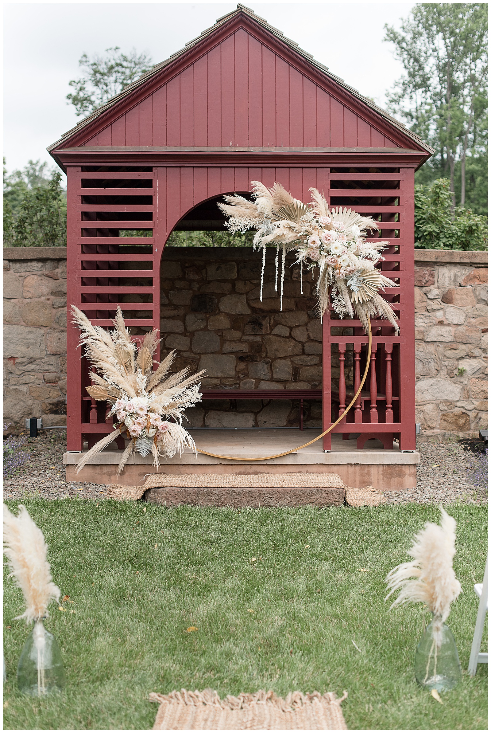 modern round archway with beautiful floral and pampas grass arrangements displayed in front of small maroon building