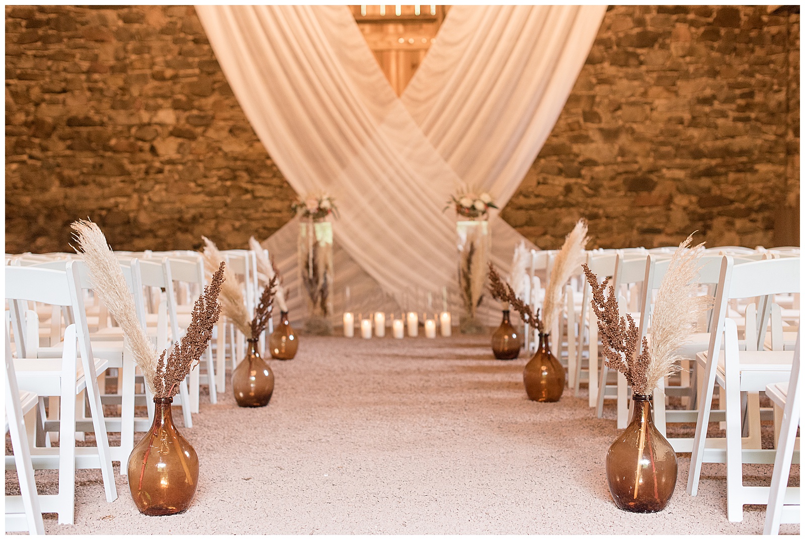 beautifully decorated stone barn wedding ceremony with rows of white chairs and white curtains on display at elizabeth furnace