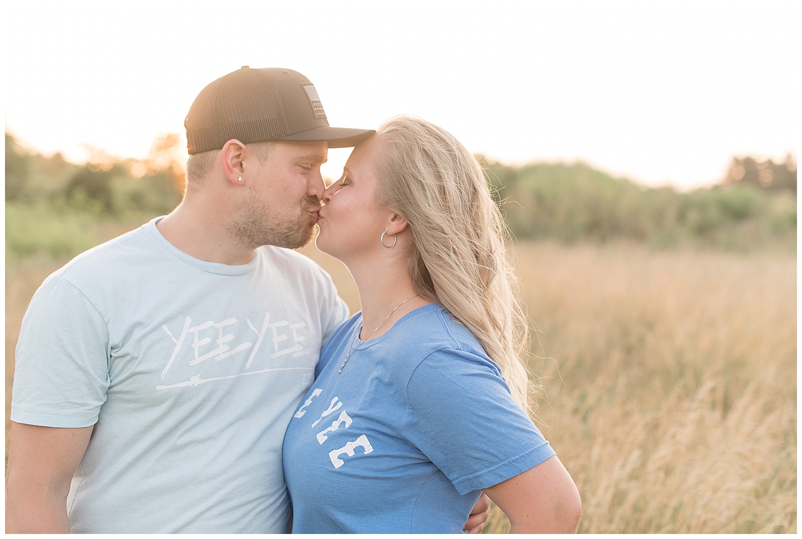 couple kissing with guy wearing baseball cap and light blue shirt and girl wears baby blue shirt by tall grasses at overlook park in lancaster pennsylvania