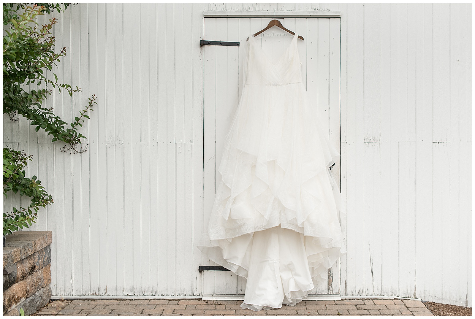 beautiful white sleeveless wedding gown displayed on wooden hanger above white wooden barn door in manheim, pennsylvania