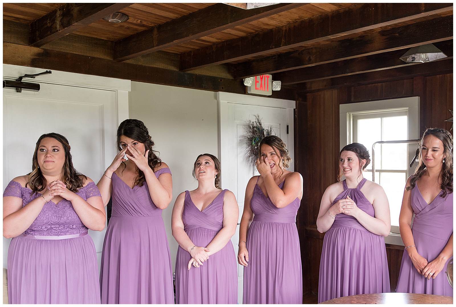 bridesmaids in lavender dresses wiping tears from their eyes as they see bride for the first time at lakefield weddings