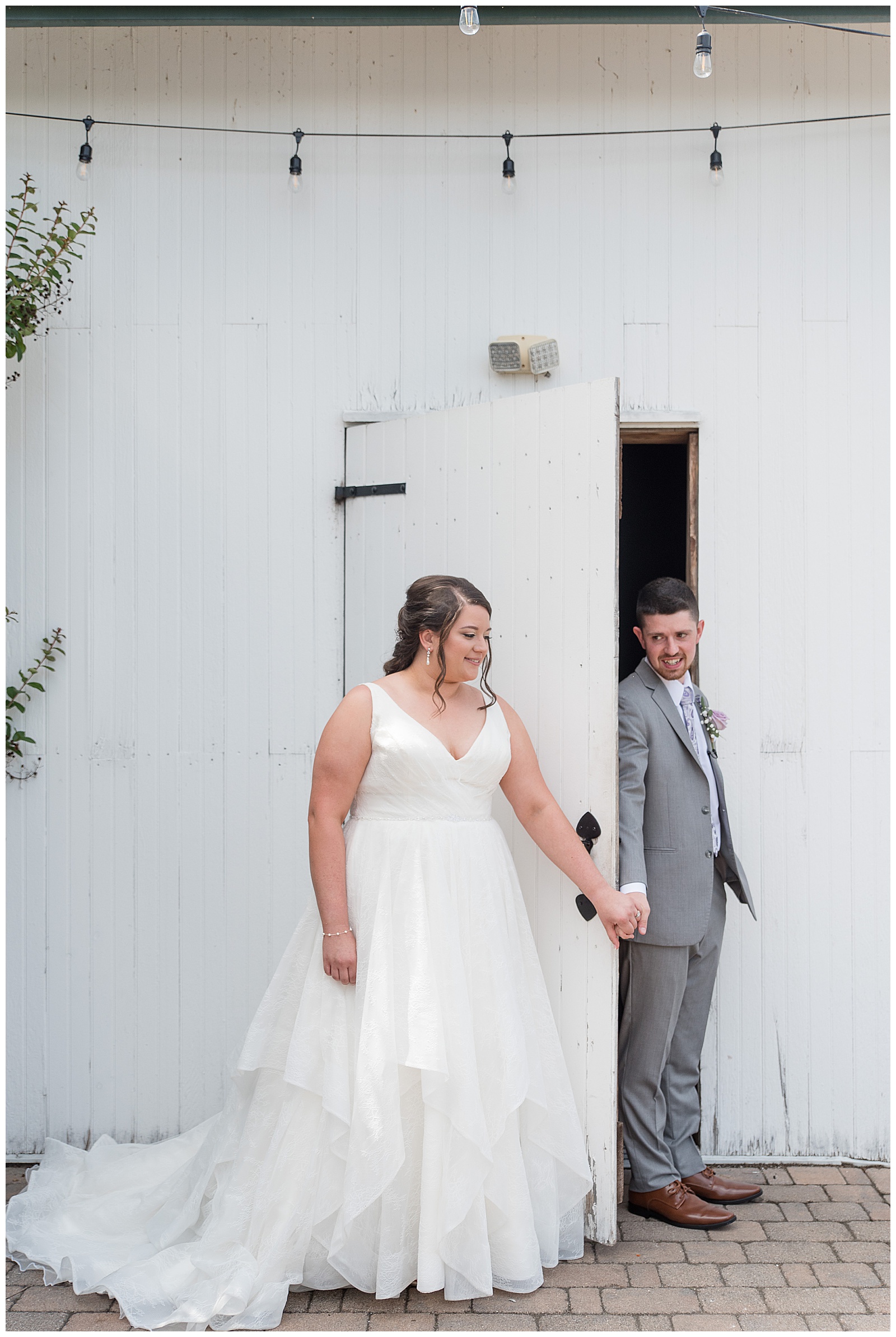 bride and groom holding hands on either side of white barn door smiling before their first look at lakefield weddings
