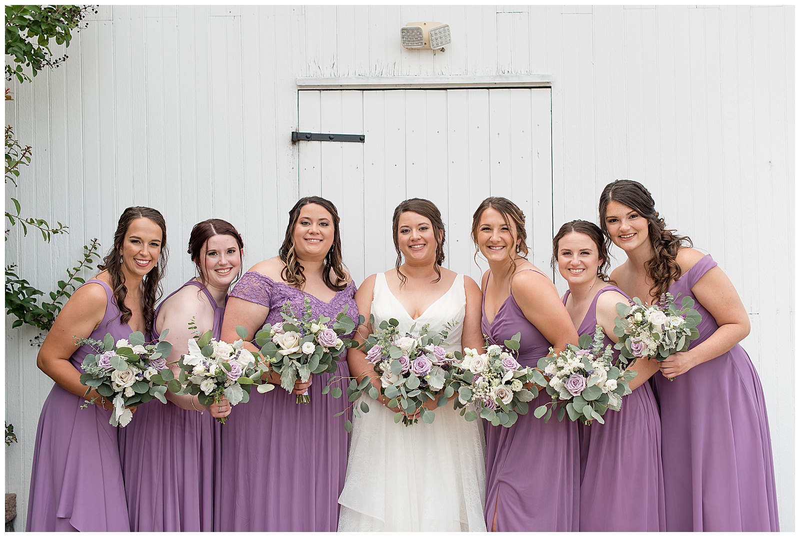 bride and bridesmaids in lavender dresses all holding bouquets in front of them and smiling in lancaster county, pennsylvania