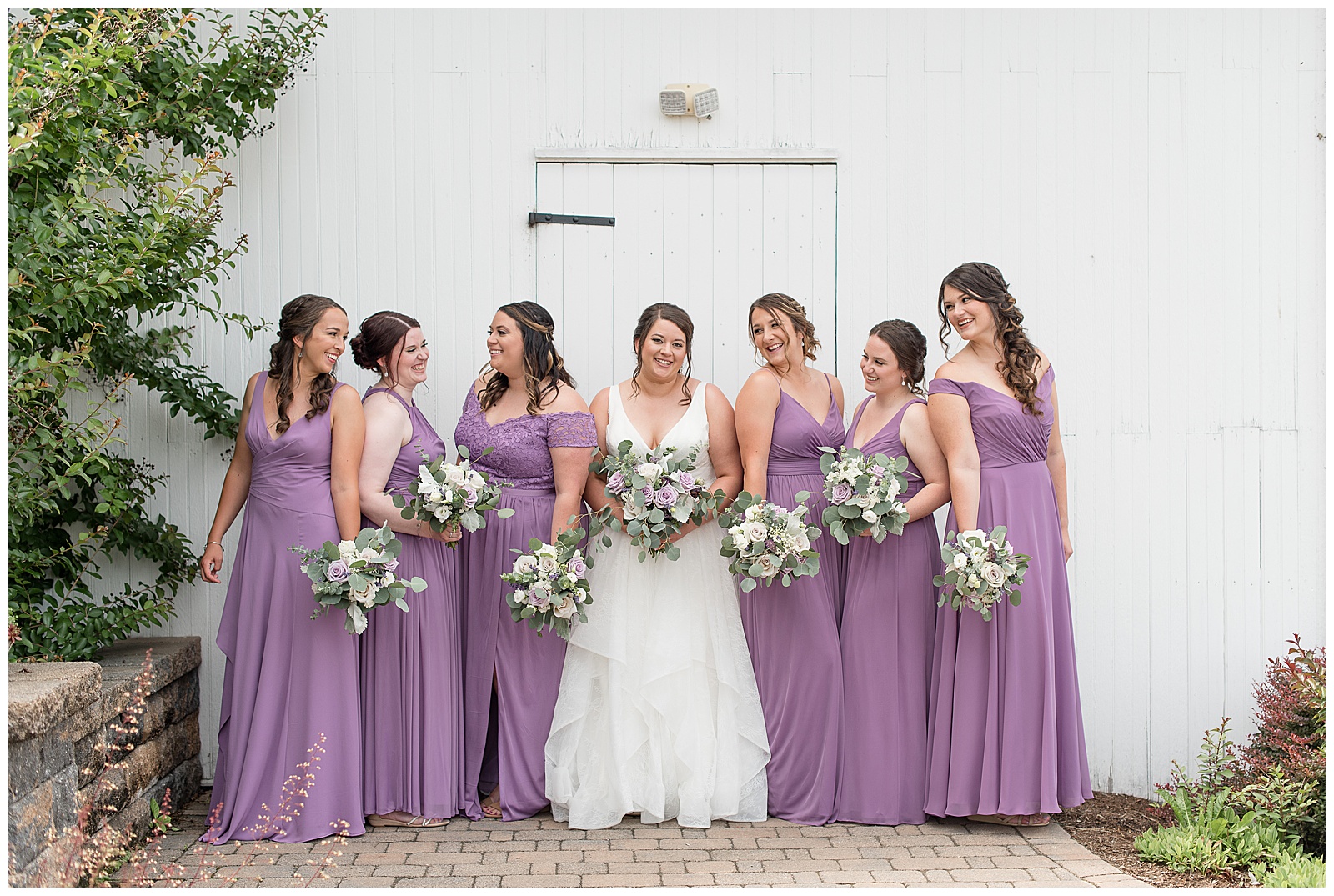 bride smiling at camera surrounded by six bridesmaids looking in different directions and smiling at lakefield weddings