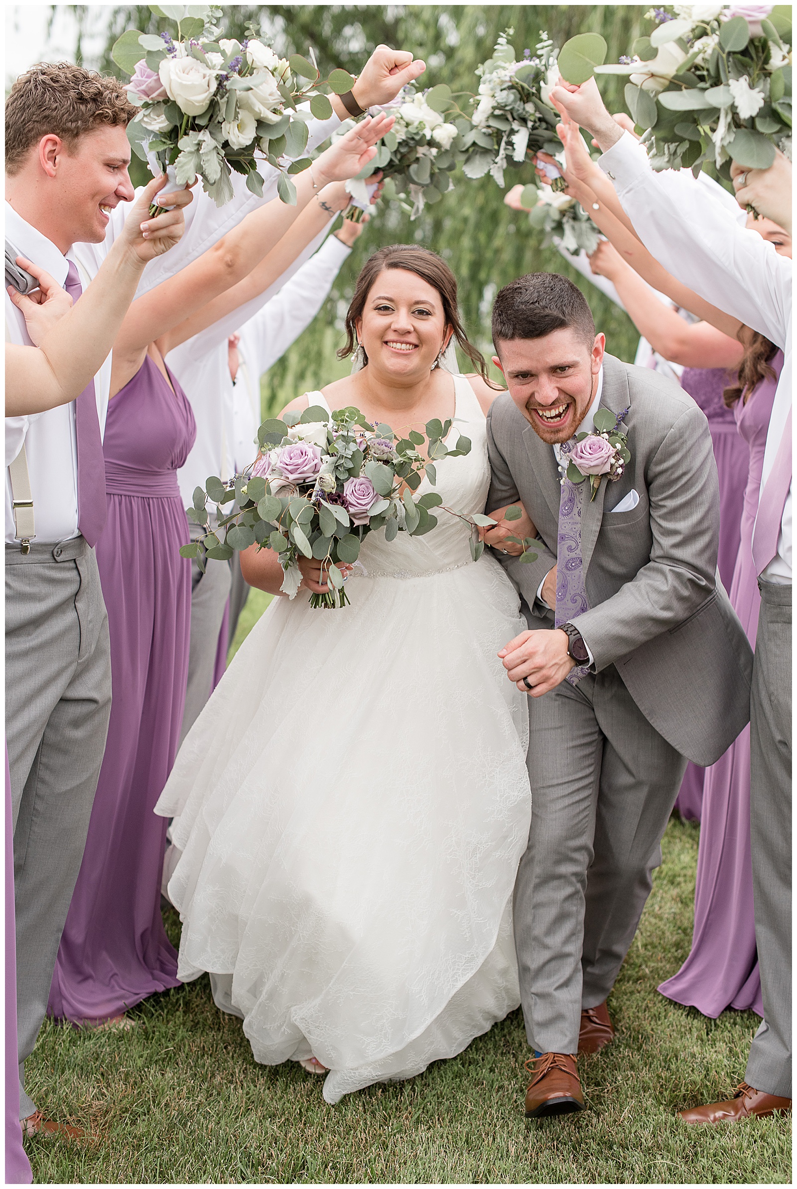 bride and groom smiling and crouched down running under the arms of their bridal party on sunny day in manheim, pennyslvania