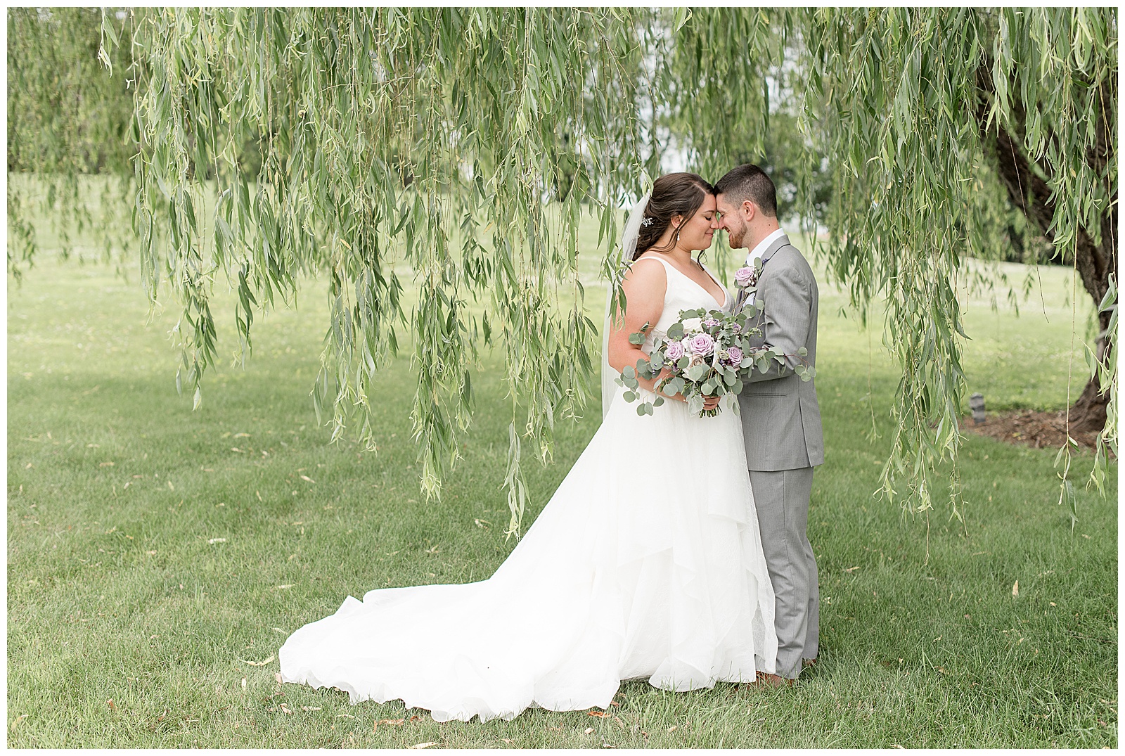 bride and groom resting their foreheads together as bride holds bouquet under willow tree at lakefield weddings