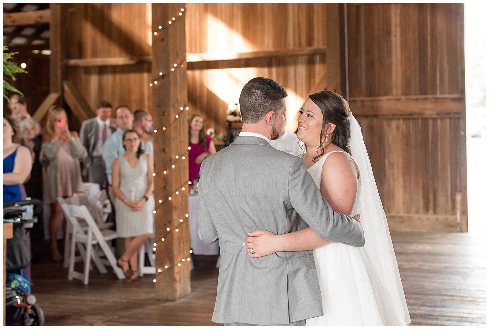 bride smiling at her groom as they do their first dance and his back is to the camera in barn venue at lakefield weddings