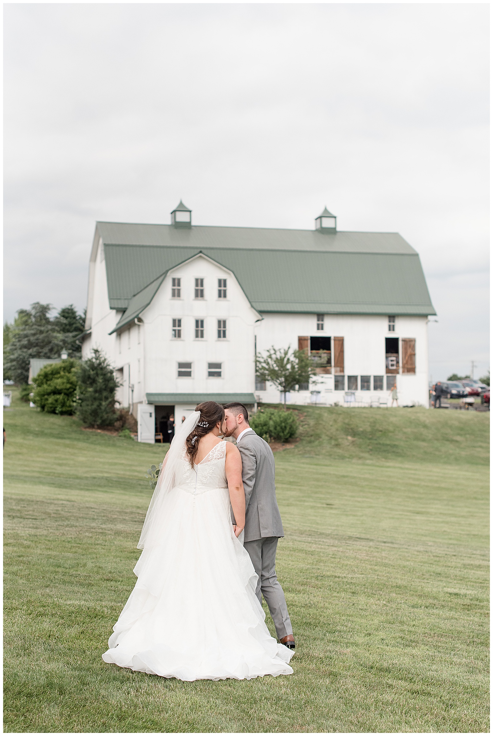 bride and groom kissing with backs toward camera and beautiful white barn behind them at lakefield weddings