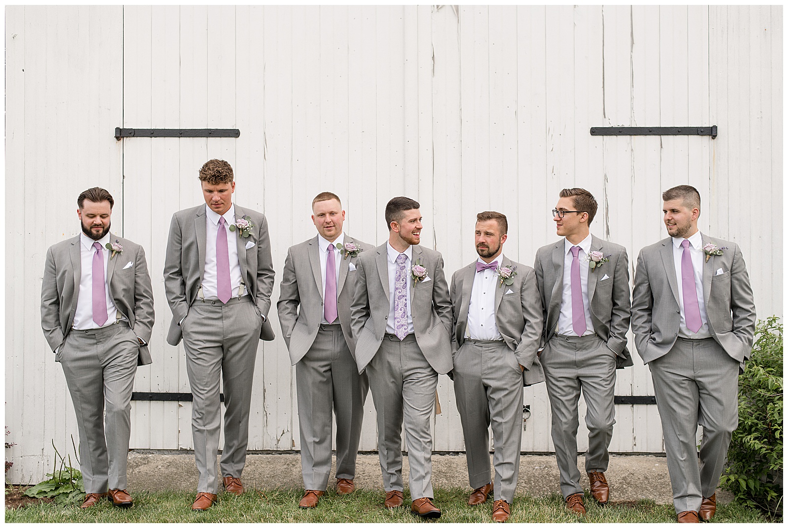 groomsmen walking in front of white barn at Lakefield Weddings
