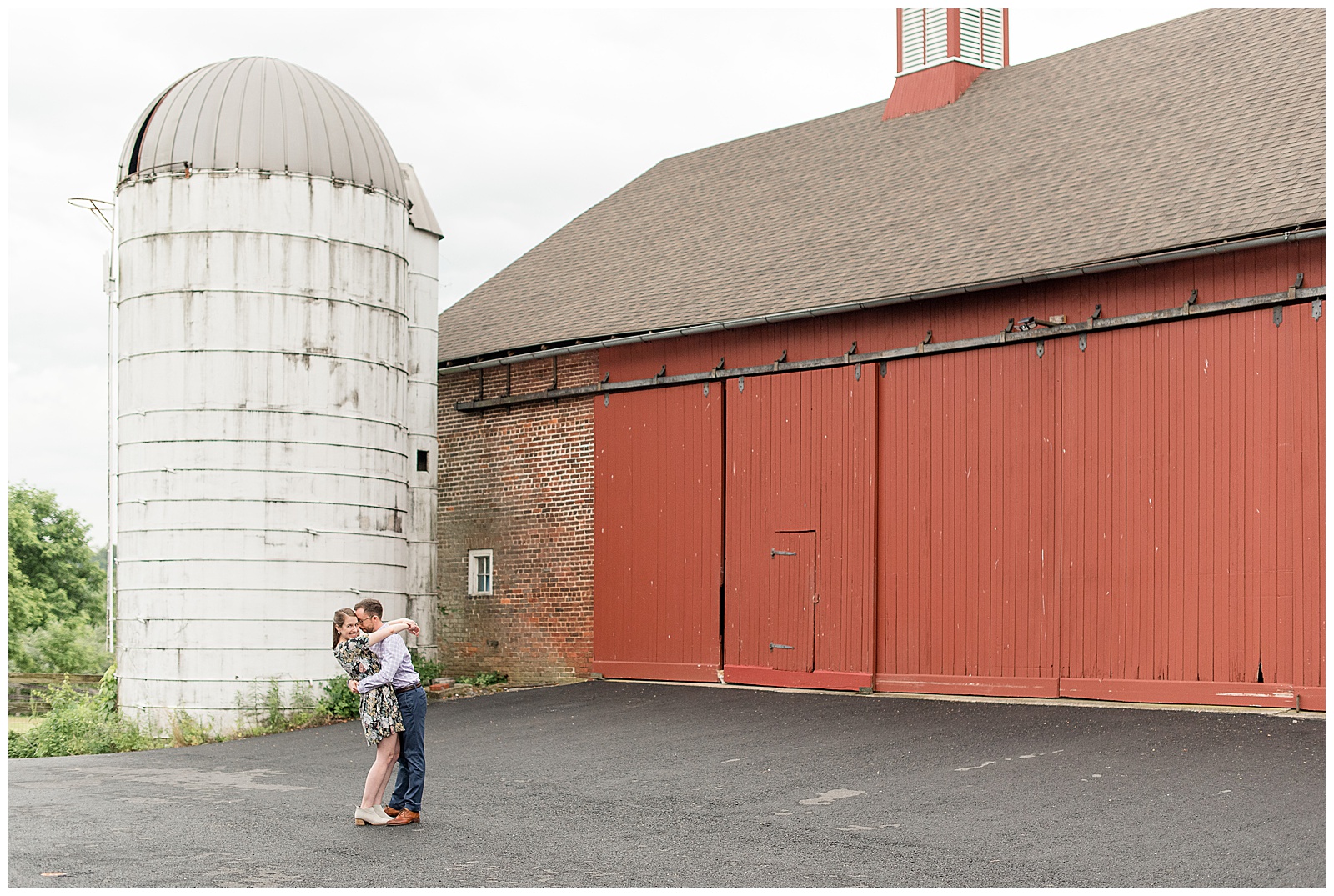 couple hugging tightly and girl tipped back slightly by white silo and red barn in mechanicsburg, pennsylvania