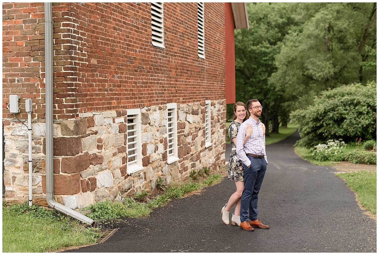 girl hugging guy from behind as they both smile next to historic stone and brick barn in central pennsylvania
