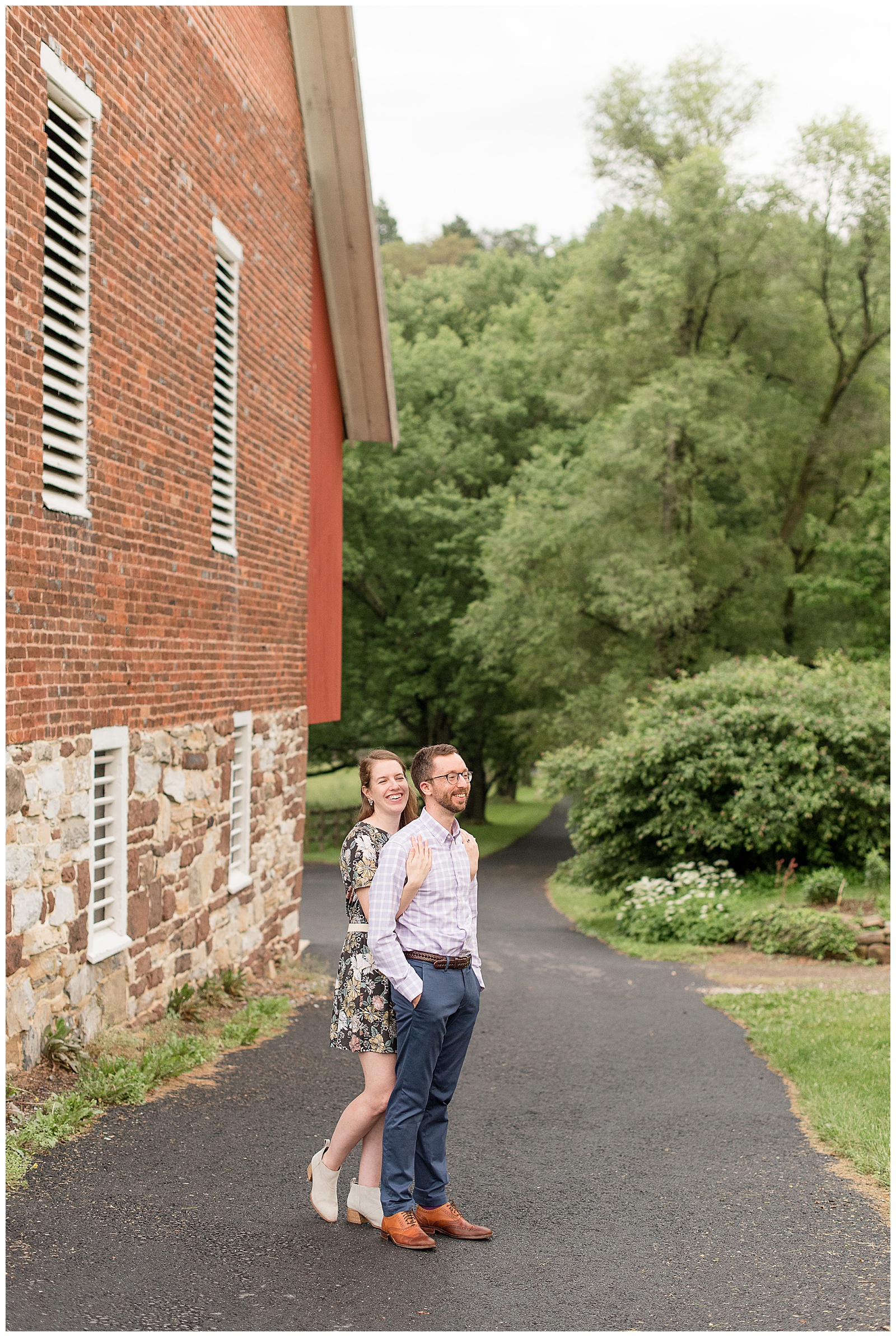 girl hugging guy from behind as they both smile next to historic stone and brick barn in central pennsylvania