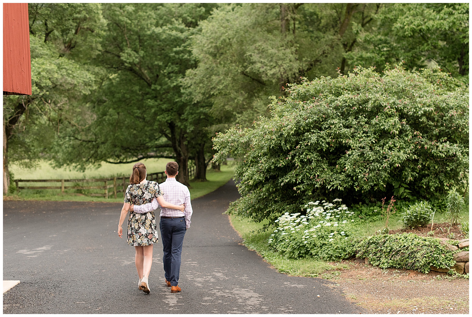 couple walks away from camera with arms wrapped around each other's lower back along landscaped paved driveway