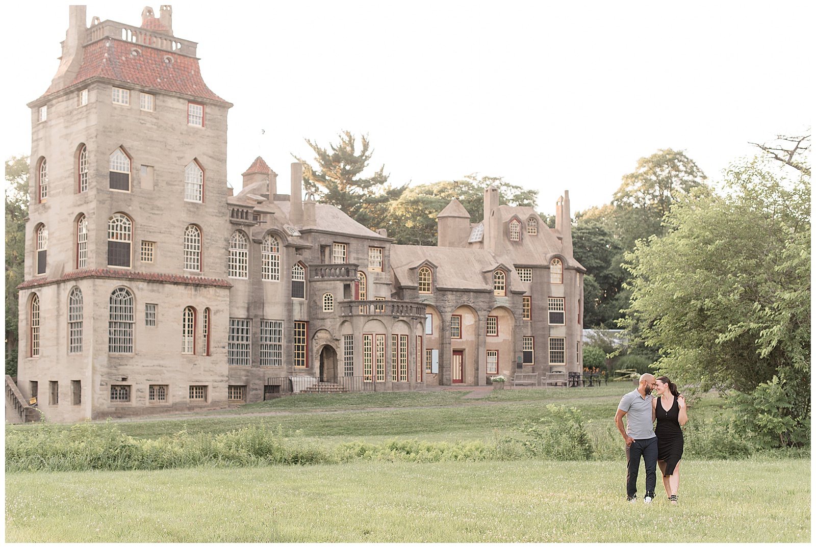 couple standing by fonthill castle, guy wearing gray polo shirt and dark pants and girl wearing black dress