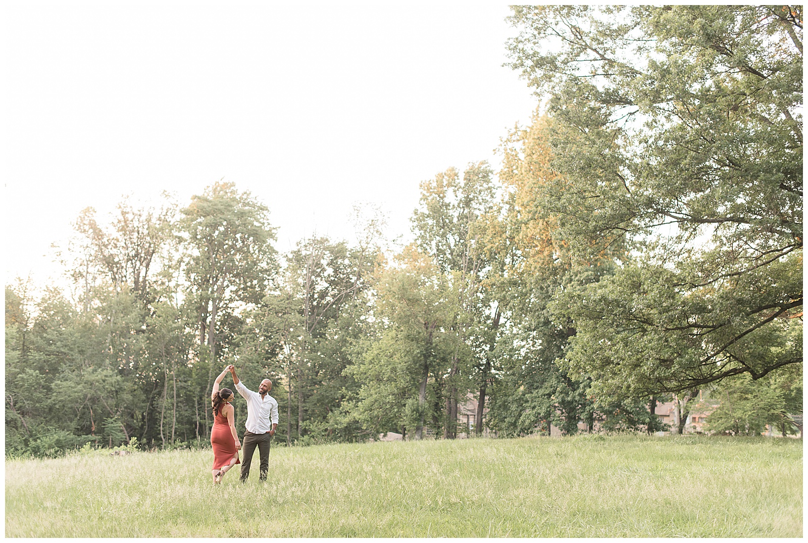 guy twirls girl in grassy field by row of trees on sunny summer evening in doylestown pennsylvania