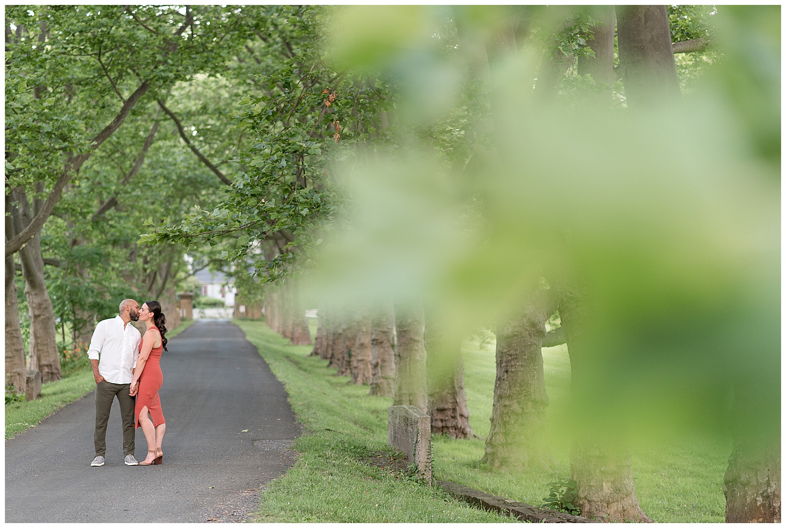 engaged couple kissing on path with closeup leaves of tree in the foreground near philadelphia pennsylvania