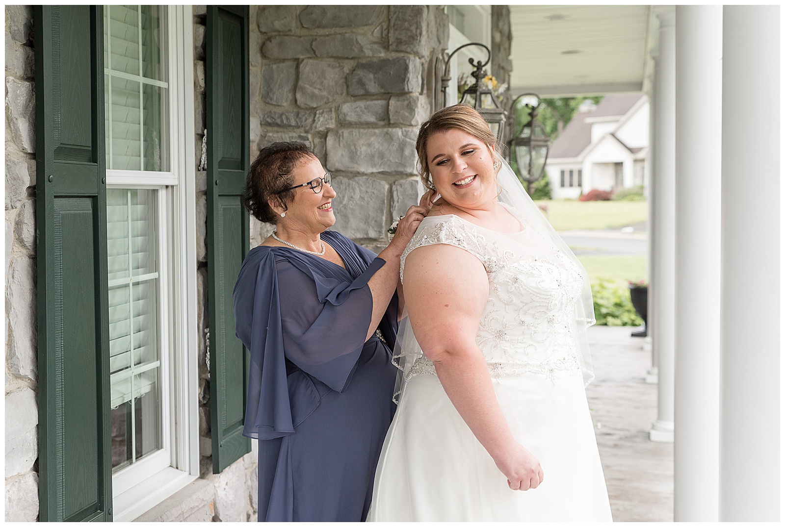 bride glances over right shoulder and smiles at her mom as she adjusts the back of her wedding gown in lancaster pennsylvania