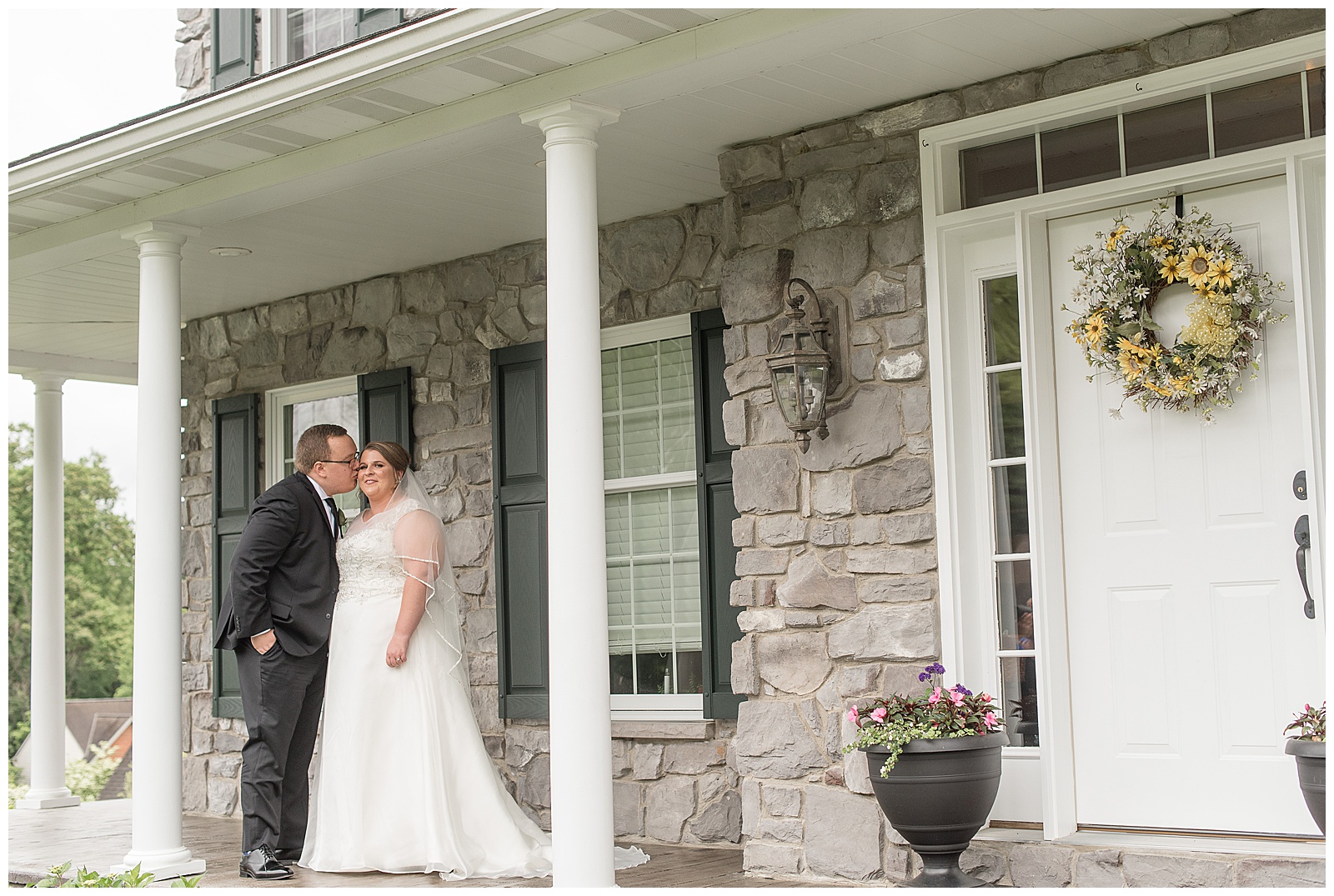 groom kisses bride on her right cheek as she smiles at camera on front porch in lancaster pennsylvania