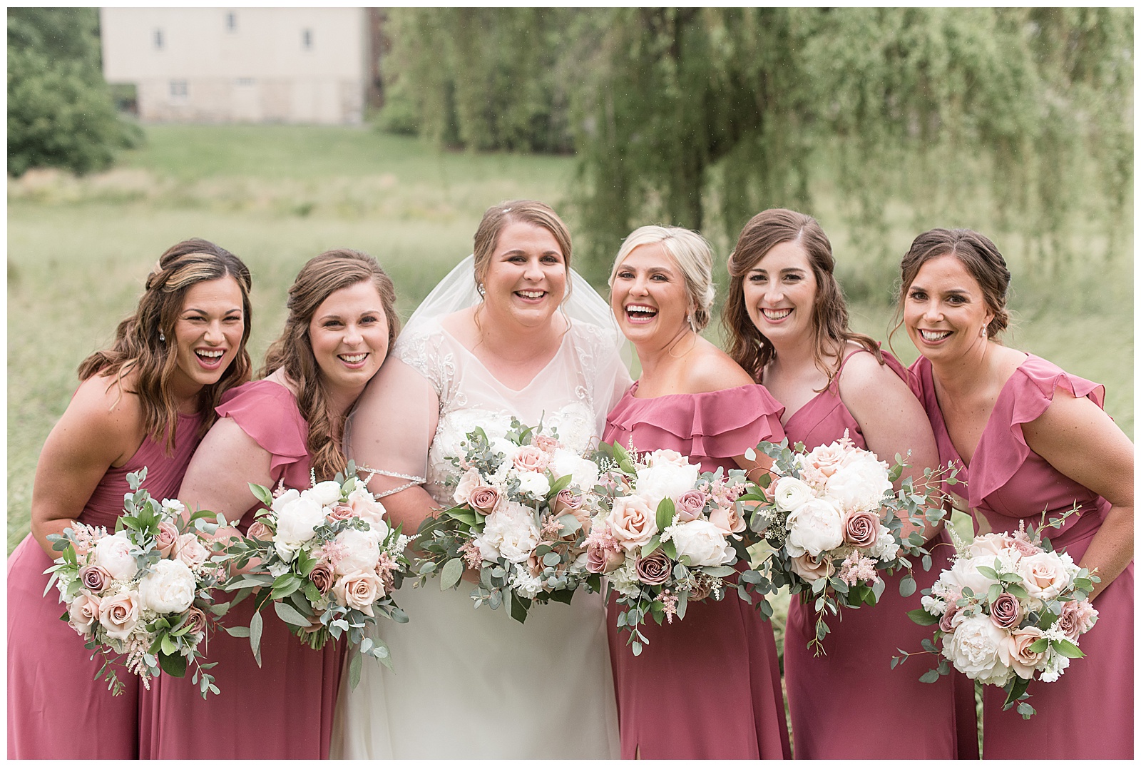 bride surrounded by five bridesmaids standing close in blush gowns holding bouquets at willows at historic strasburg