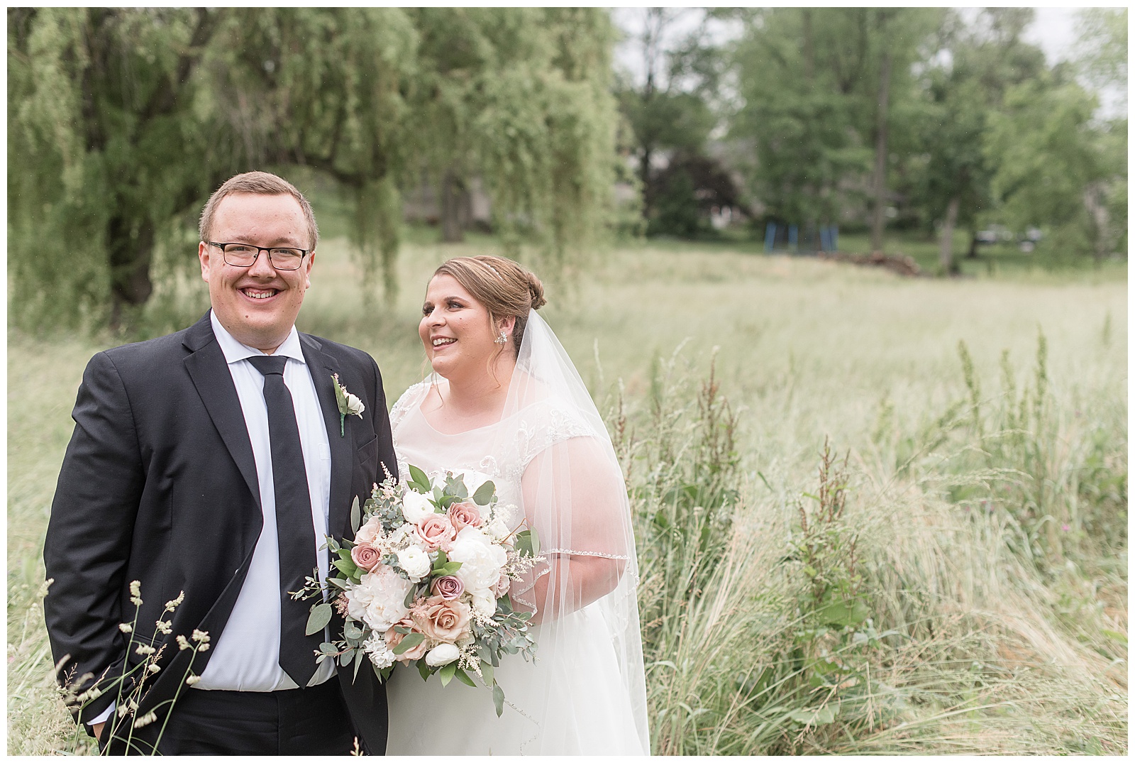 groom smiling as bride looks at her groom and smiles beside tall grasses and willow tree at willow at historic strasburg