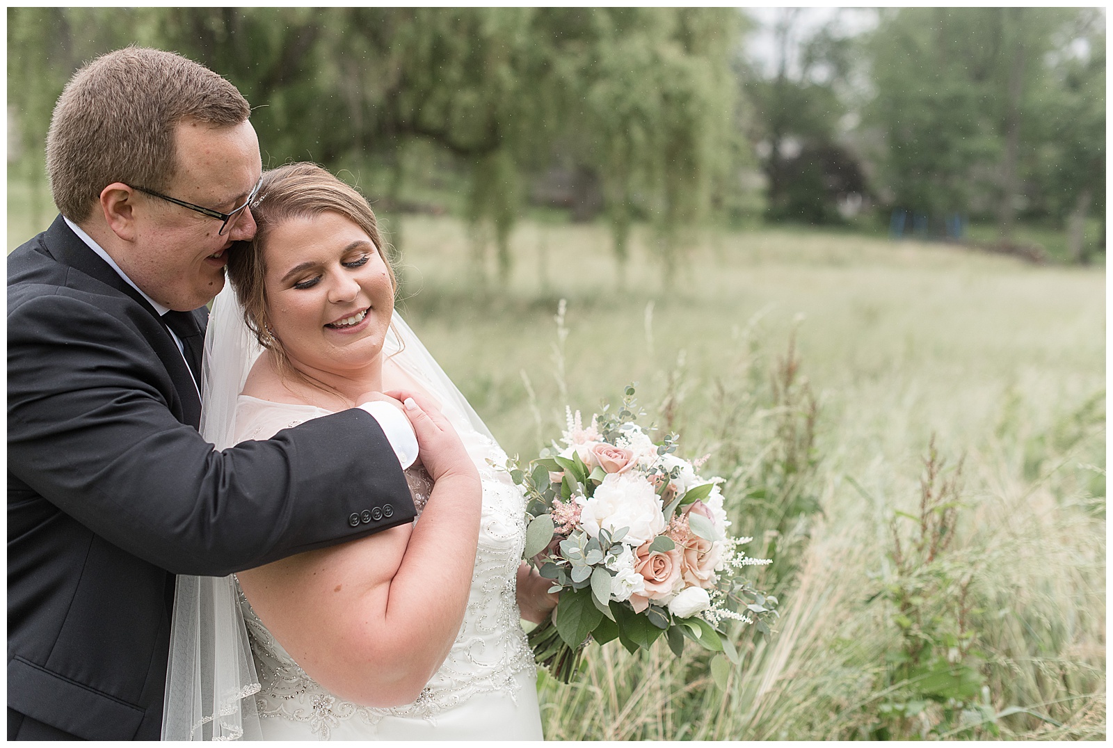 groom hugs bride from behind as they both look down smiling by tall grasses in lancaster pennsylvania