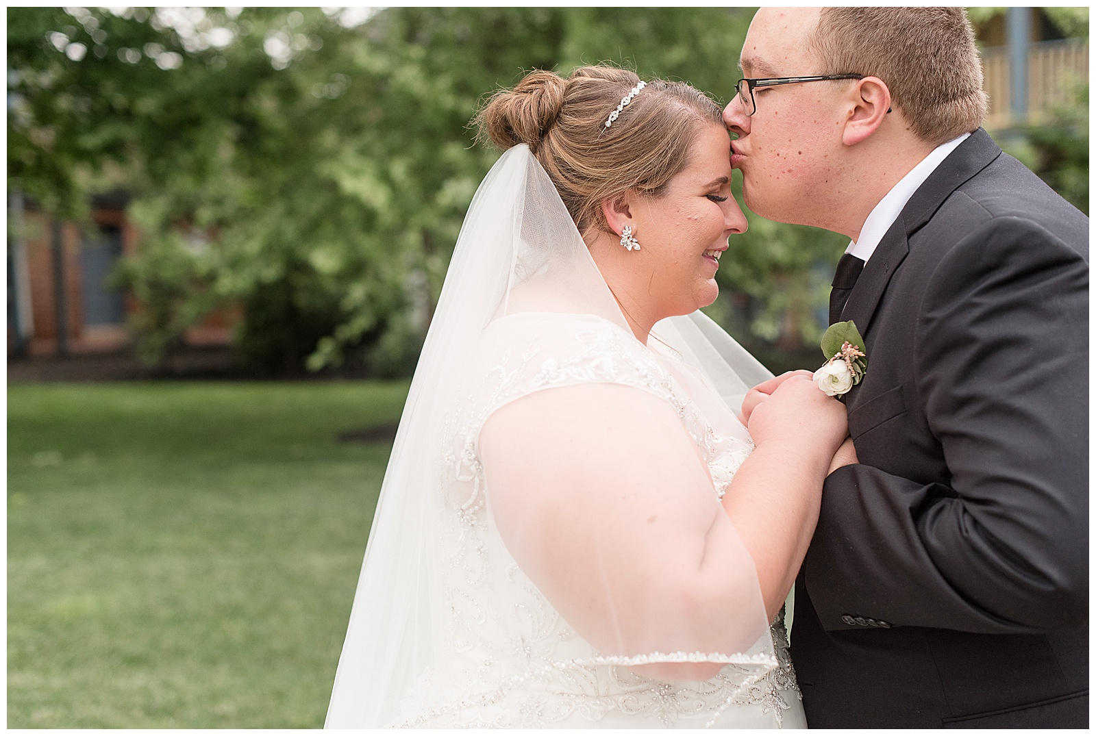 close up of groom kissing bride on her forehead as she smiles with her eyes closed and their hands joined together in strasburg pennsylvania