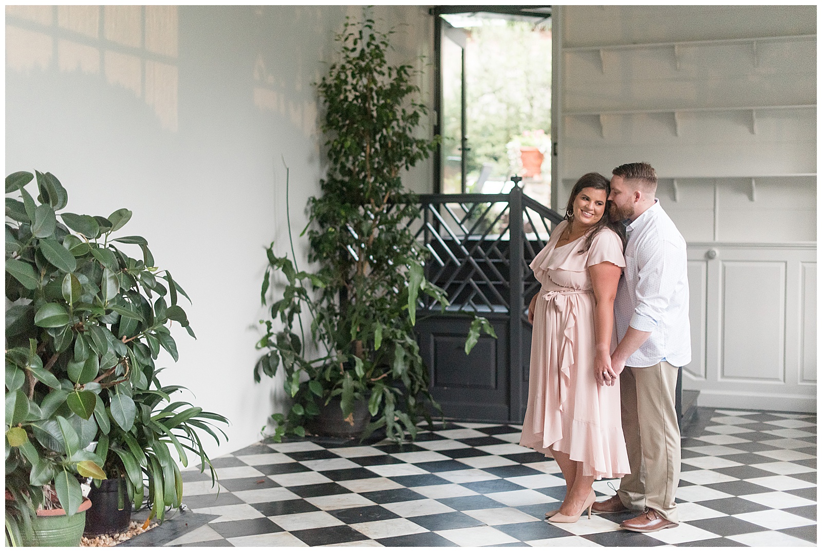guy standing behind girl as she looks down smiling inside white room with checkered floors and houseplants in lancaster pennsylvania