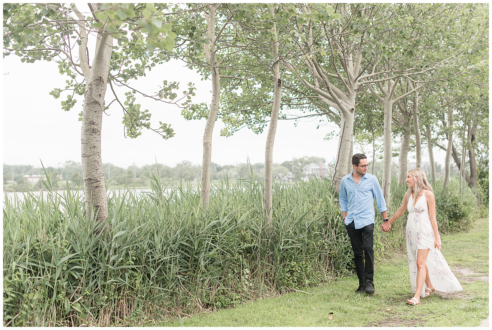 couple holding hands and smiling at each other while walking along tall grasses in bayhead new jersey