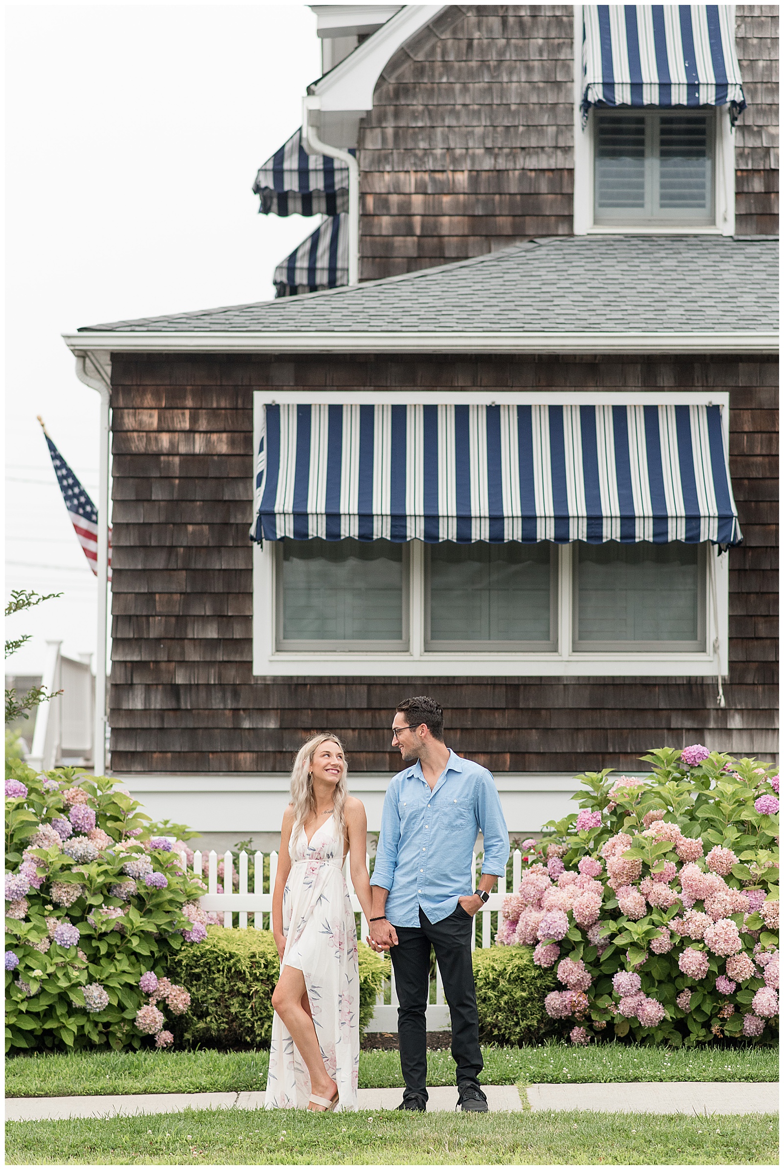 couple smiling at each other in front of beach home and beautiful pink hydrangea bushes on east coast