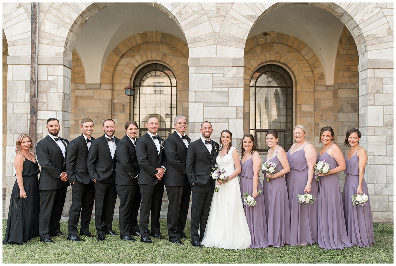 bridal party smiling at camera in front of stone arches