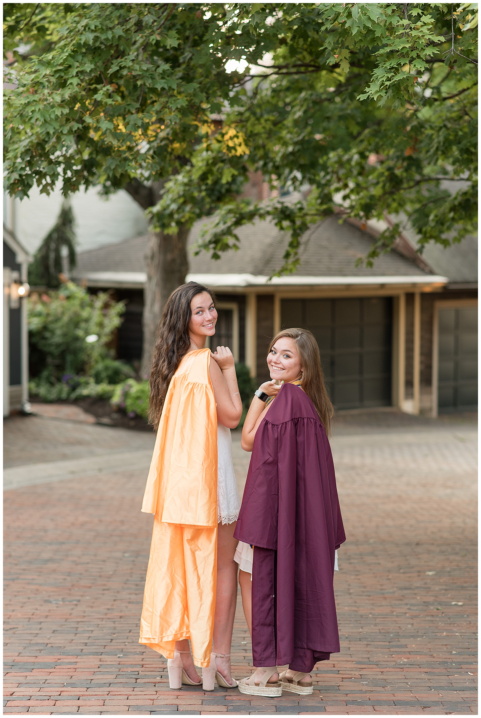 two senior girls with graduation gowns draped over shoulders looking back and smiling at camera in lancaster city