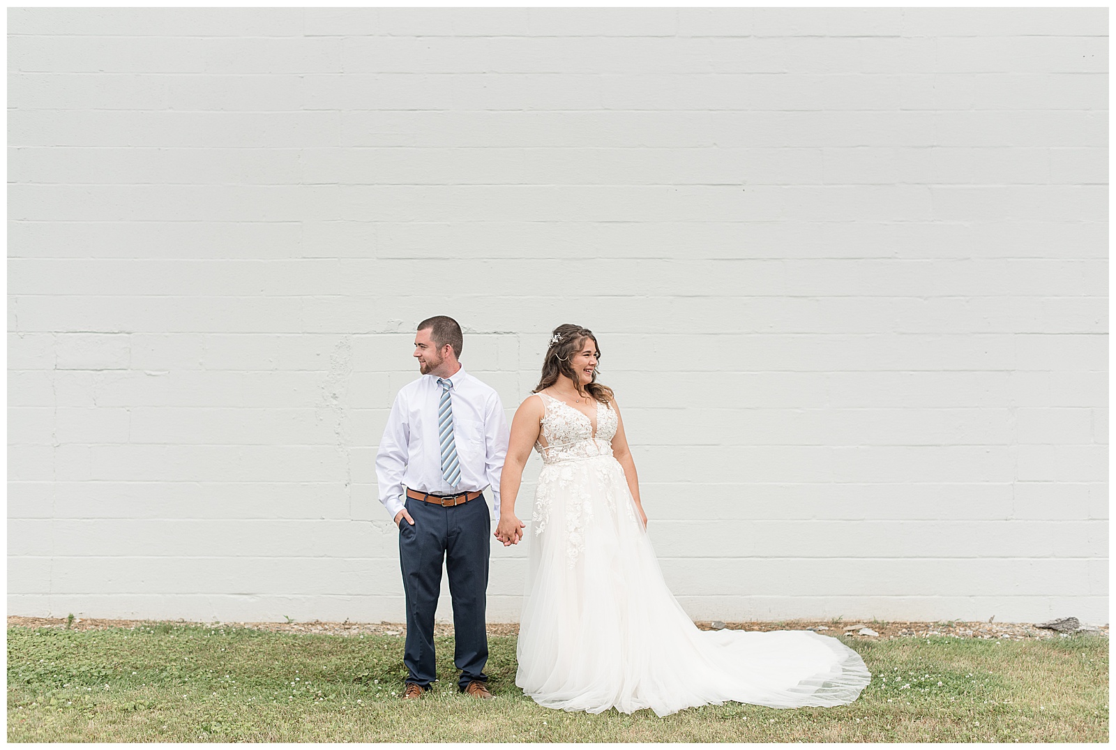 bride and groom holding hands looking away from each other in front of white wall