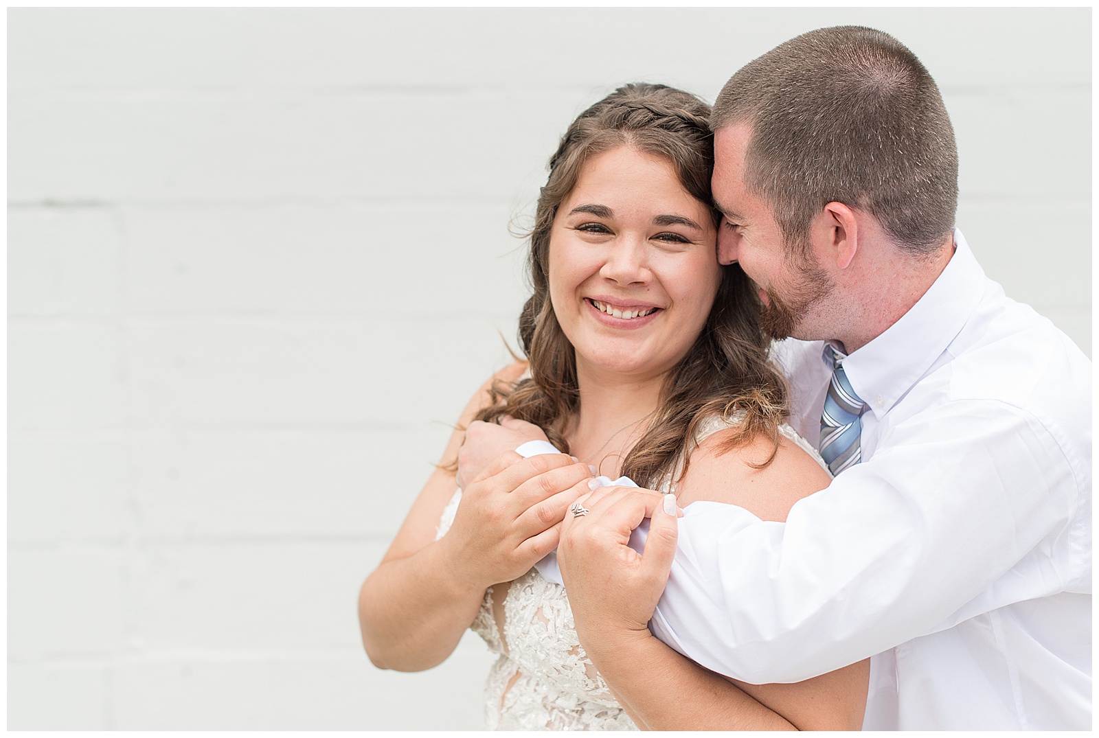 groom's arms wrapped around bride as she smiles at camera