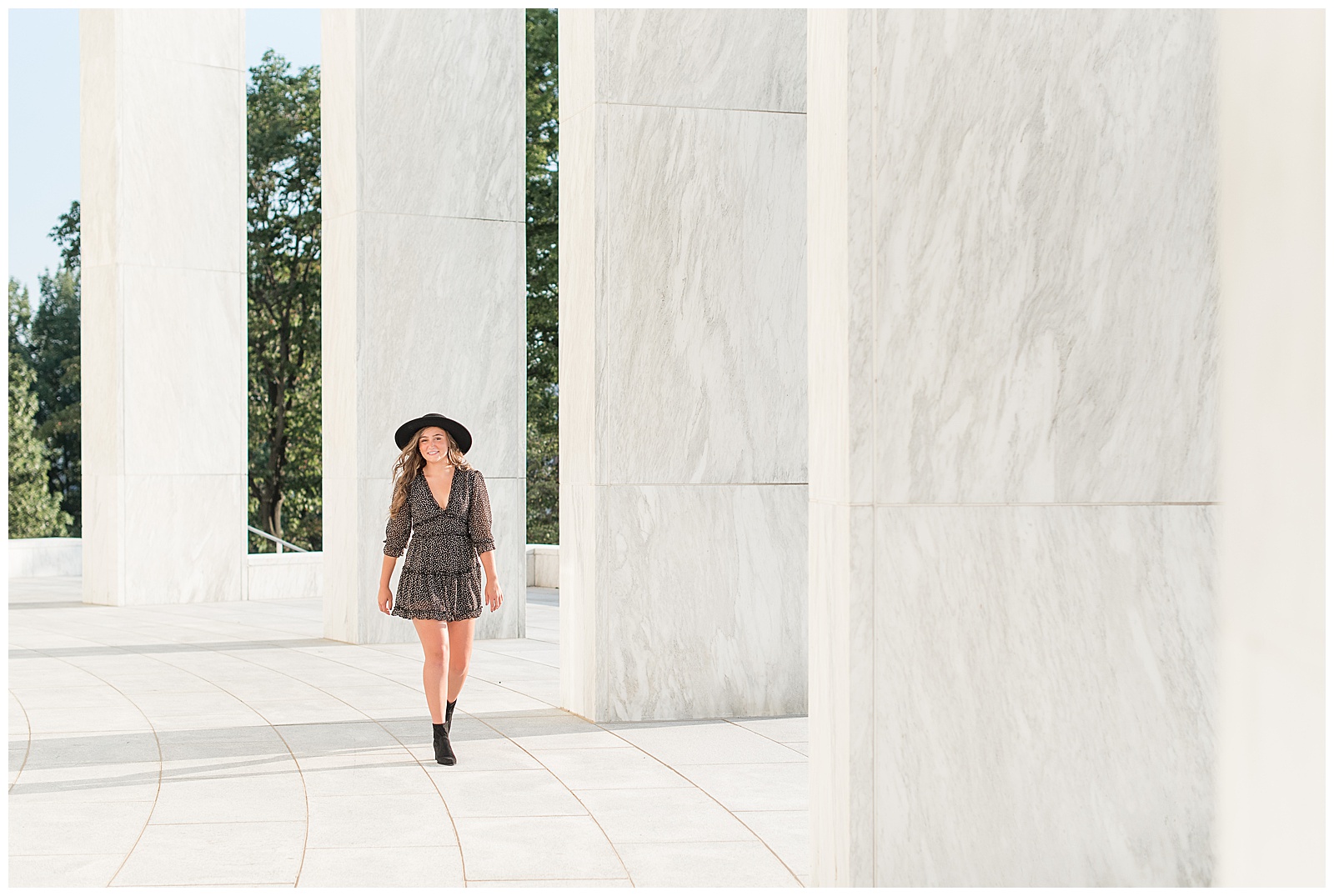 senior girl in black dress and black hat walking by large white pillars at founders hall in hershey pennsylvania
