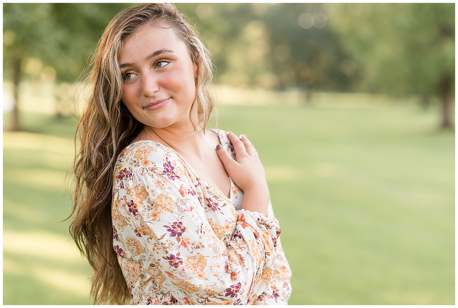 close up of senior girl in colorful floral top looking over her right shoulder with her right hand on left shoulder at founders hall