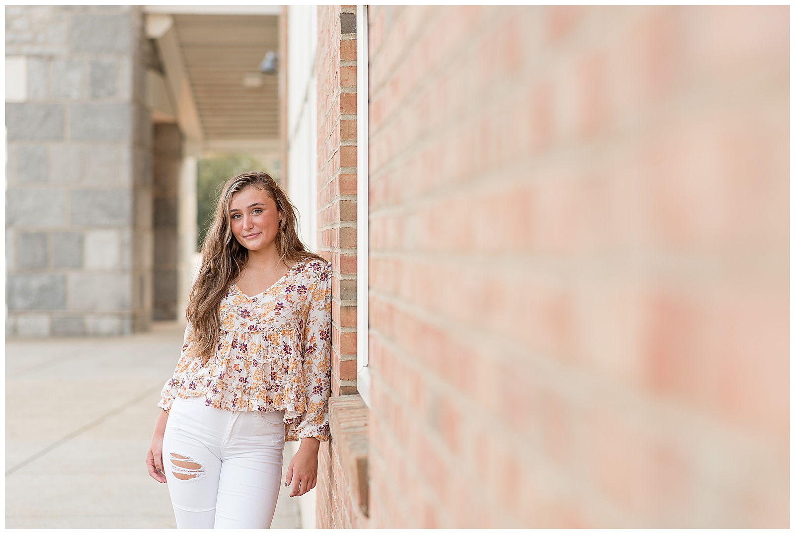 senior girl leaning against brick building and smiling at camera at founders hall in hershey pennsylvania