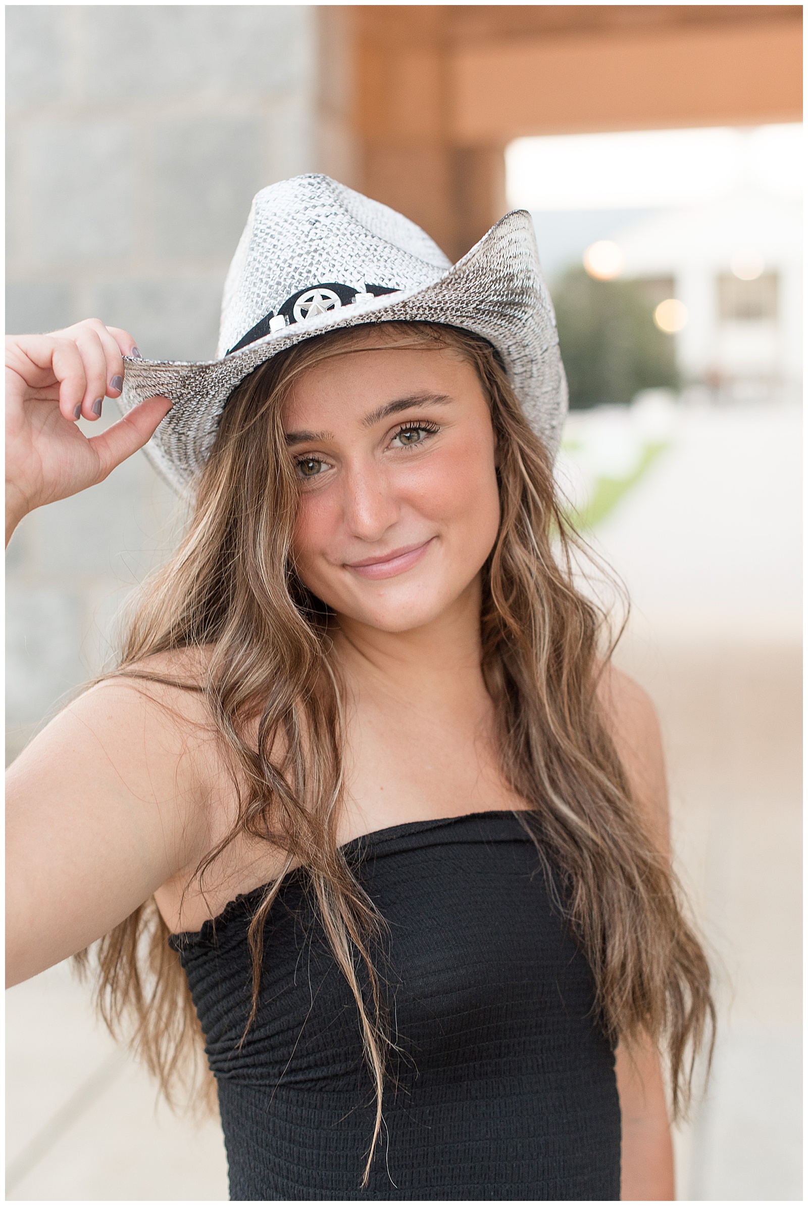 close up photo of senior girl wearing white cowboy hat with her right hand tipping the hat as she smiles in hershey pennsylvania