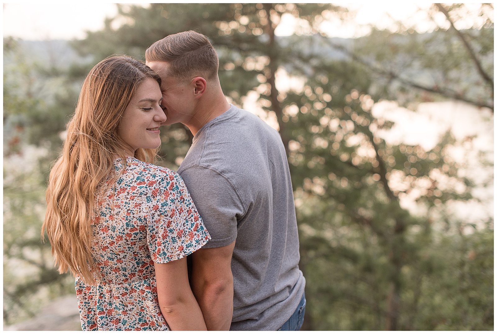 engaged couple with their backs toward camera as guy leans in and kisses girl on her left cheek and she smiles at pinnacle overlook