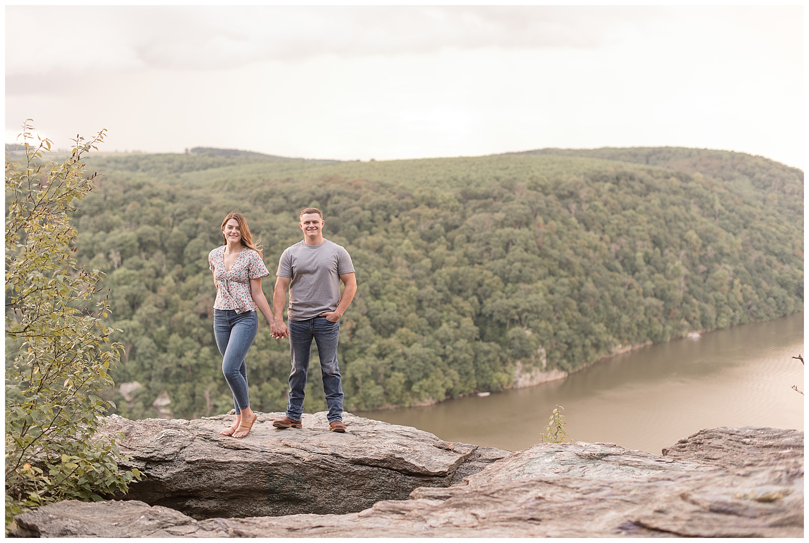 engaged couple holding hands smiling atop large rock overlooking susquehanna river at pinnacle overlook